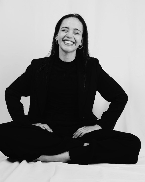 Z’nita Lori’an Young, seated, in a black suit, laughing.